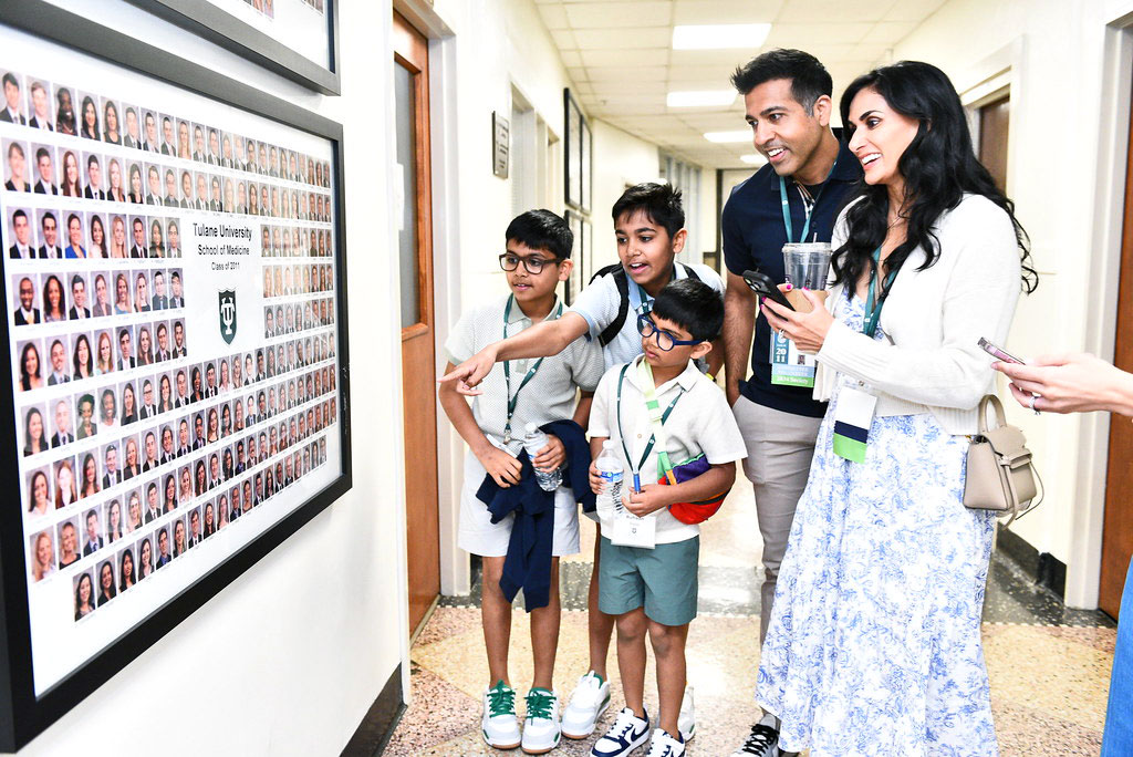 Family with two boys points at a large framed photo collage of student portraits in a hallway.